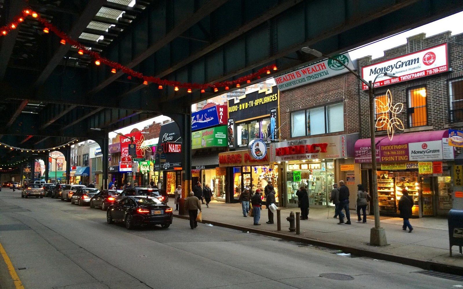 An elevated subway line running above a wide avenue, adults crossing beneath